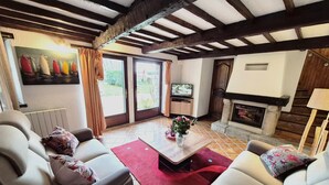 A living room with a fireplace, a television, and a large window with curtains. - Gîte de Kerberso near Paimpol in Côtes-d'Armor (Pléhédel)