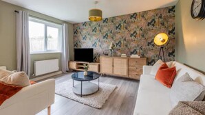 A living room with a sofa, a coffee table, a TV, a cabinet, and a patterned wall. - Charming Whitehurst Drive Nest in Manchester (Manchester)