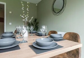 Una mesa de comedor con platos grises y copas de vino, un jarrón con flores blancas y un espejo en la pared.