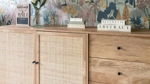 A wooden cabinet with a woven front panel and drawers, a floral wallpaper background, and three books titled 'Family', 'Aesthetic', and 'Abstract'. - Charming Whitehurst Drive Nest in Manchester (Manchester)