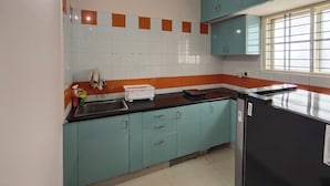 A kitchen with teal cabinets, a black countertop, and a window with blinds. - Ramamurthy/sleeps6/2bedroom/tv/wifi (Bengaluru)