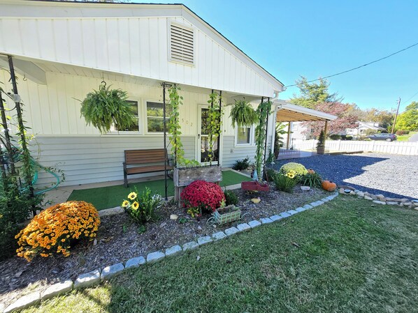 A house with a porch, a bench, and a garden with various plants and flowers.