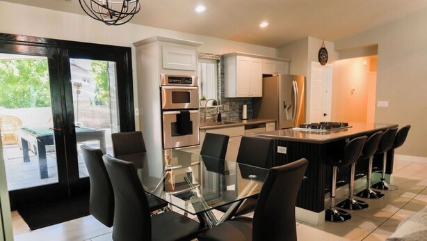A modern kitchen with white cabinets, stainless steel appliances, and a glass dining table with black chairs. - Delightful 3-bedroom house in Flagstaff (Flagstaff)