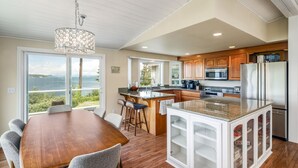 A modern kitchen with a large island, wooden cabinets, and a view of the outdoors. - Waterfront Home with Game Room, Fireplaces, Kayaks, AC and Private Beach Access (Camano)