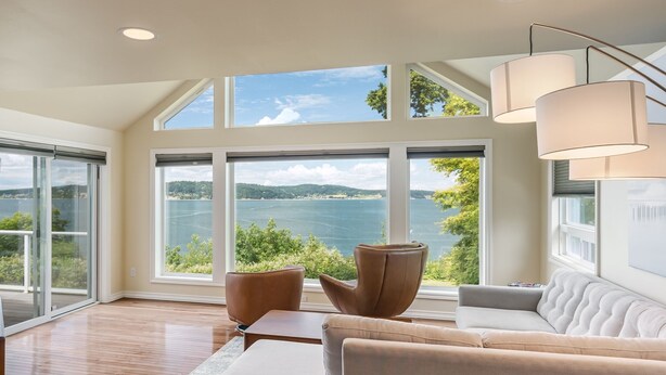 A modern living room with a large window, a sofa, a coffee table, and two chairs. - Waterfront Home with Game Room, Fireplaces, Kayaks, AC and Private Beach Access (Camano)