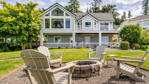 A two-story house with a front deck, a fire pit, and outdoor seating. - Waterfront Home with Game Room, Fireplaces, Kayaks, AC and Private Beach Access (Camano)