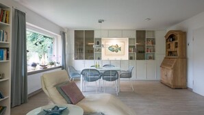 Amplia sala de estar con un sofá moderno, una mesa de comedor con sillas, una estantería y un mueble de madera.