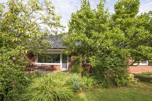 Un jardin avec une terrasse, un mur en briques et une pergola.