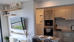 Una cocina moderna con electrodomésticos integrados, una zona de comedor con mesa y sillas, y un televisor de pantalla plana montado en la pared.