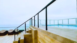 Un espace aménagé au bord de la piscine, avec des marches menant à celle-ci, une rambarde en verre et une vue sur la mer.