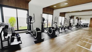 Une salle de sport équipée de divers appareils d’exercice, dotée de grandes fenêtres et d’un plancher en bois.