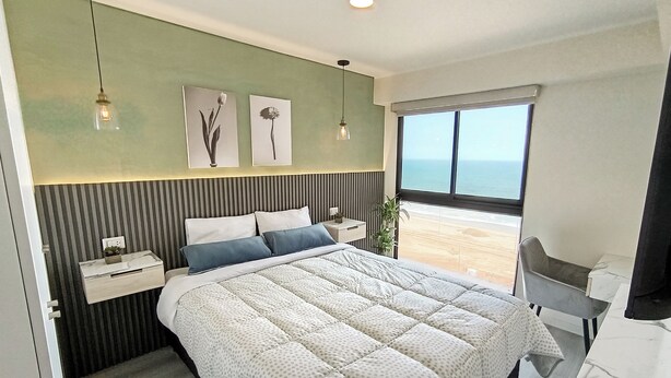 Une chambre à coucher moderne avec un grand lit, une table de chevet, un bureau et une vue sur la plage.