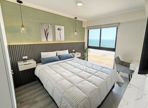 Une chambre à coucher moderne avec un grand lit, une table de chevet, un bureau et une vue sur la plage.