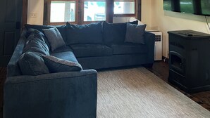 Ein gemütliches Wohnzimmer mit Holzboden, einem großen Fenster, einer Couch und einem Kaminofen.