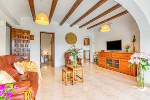 A living room with a leather sofa, wooden coffee table, and a TV on a wooden cabinet. - Villa 'El Horreo Xabia' with Mountain Views, Wi-Fi, and Air Conditioning (Panorama)