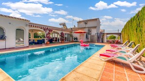 A swimming pool with lounge chairs, a pink flamingo float, and a building with arches and a tiled roof.