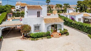 A white villa with a tiled roof, a satellite dish, and a swimming pool.