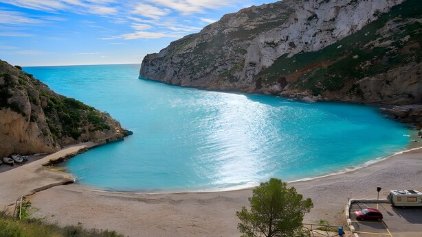 A coastal landscape with a beach, cliffs, and a clear sky.