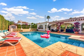 A swimming pool with lounge chairs, a flamingo float, and a building with arches and potted plants. - Villa 'El Horreo Xabia' with Mountain Views, Wi-Fi, and Air Conditioning (Panorama)