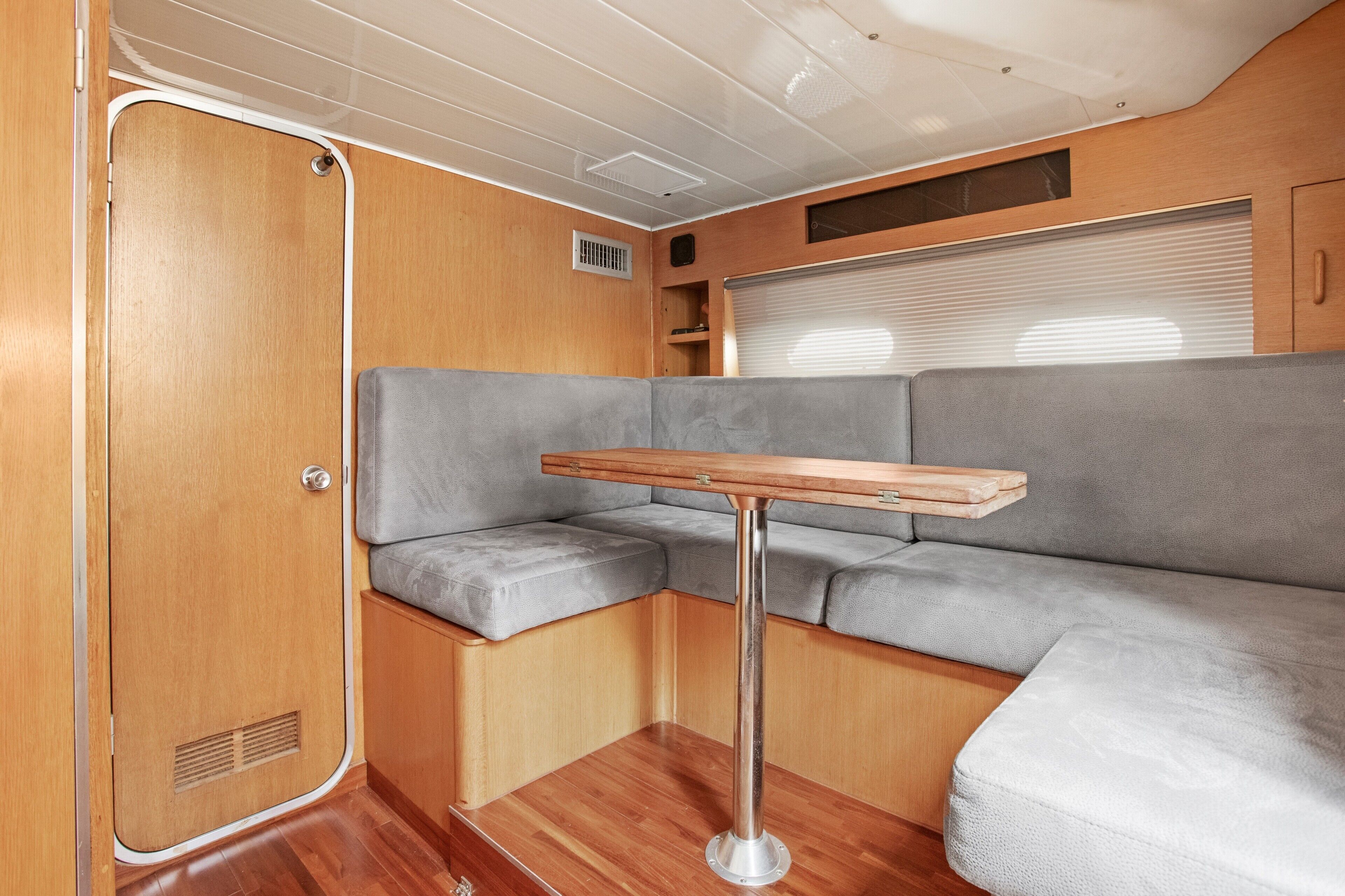 A compact RV interior with a wooden door, a cushioned seating area, and a small table.