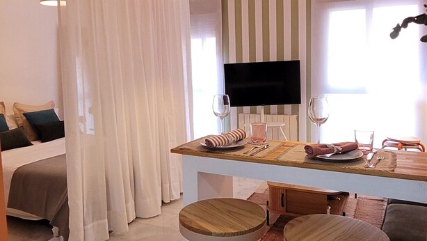 A modern hotel room with a dining area, a TV, and a bed.