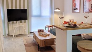 A modern living room with a TV, a dining area with a table and chairs, and a kitchen counter.