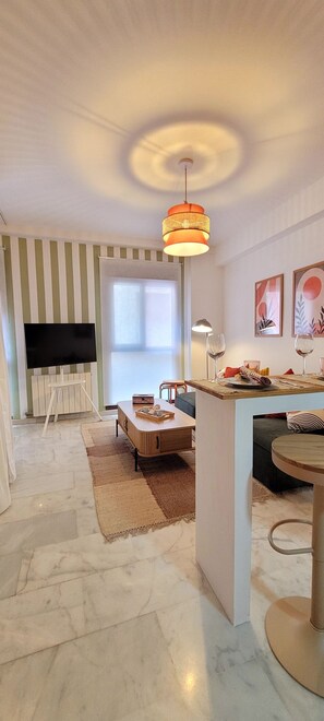 Una sala de estar moderna con televisor, una zona de comedor con mesa y sillas, y una encimera de cocina.