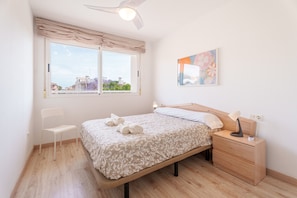A bedroom with a bed, a chair, a nightstand, a ceiling fan, a window with curtains, and a wall-mounted artwork.