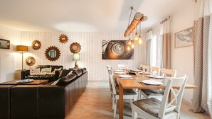 Un comedor con una larga mesa de madera, sillas blancas y un sofá negro.
