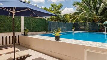 An outdoor pool area with lounge chairs, a blue umbrella, and a clear sky.