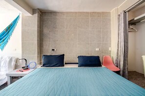 A bedroom with a bed, two pillows, a bedside table with a lamp, a chair, and a hammock.