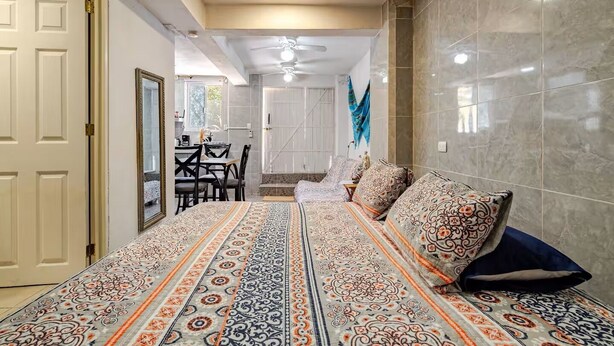 Ein Schlafzimmer mit einem gemusterten Bettüberwurf, einem Sofa mit passenden Kissen, einem Essbereich mit Tisch und Stühlen und einem Badezimmer mit Dusche und gefliesten Wänden.