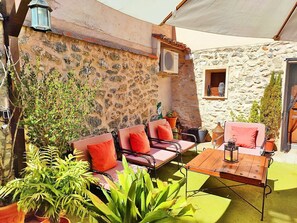 Eine Terrasse im Freien mit Steinmauern, einem Holztisch und rotem Sitzkissen.
