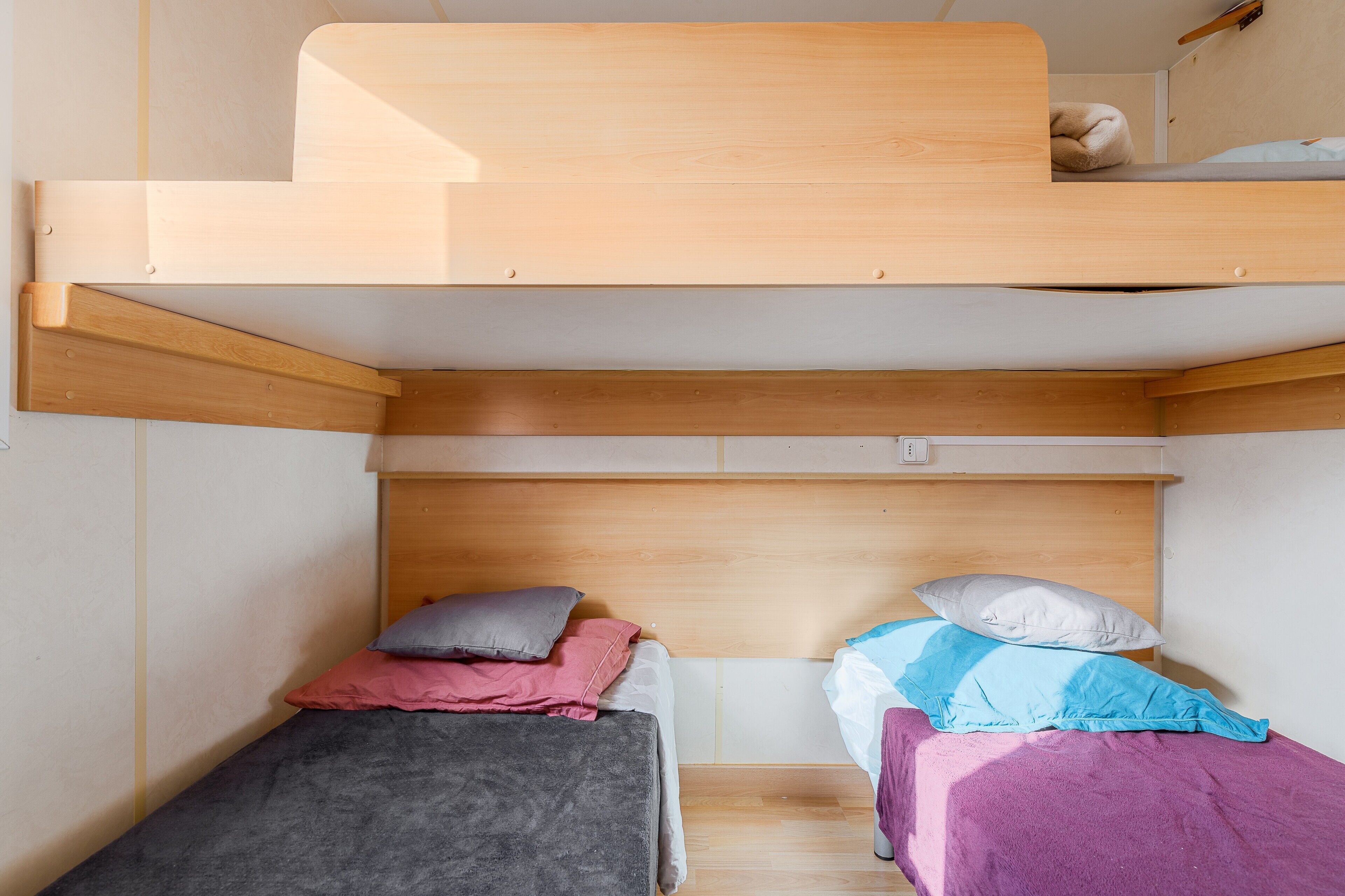 Een stapelbed met een houten hoofdbord, twee eenpersoonsbedden eronder, en een klein houten plankje.
