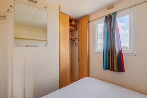 Une chambre à coucher avec un lit, une armoire, un miroir et une fenêtre avec des rideaux.
