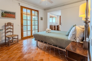 A bedroom with a bed, a chair, a lamp, a window, and a door.