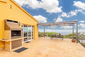 A patio with a grill, outdoor seating, and a view of the landscape.