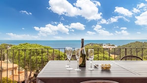 A table with a bottle and glasses on a balcony overlooking a scenic view. - Holiday Home 'Villa La Veleta On Costa Brava' with Sea View, Private Pool and Wi-Fi (Begur)