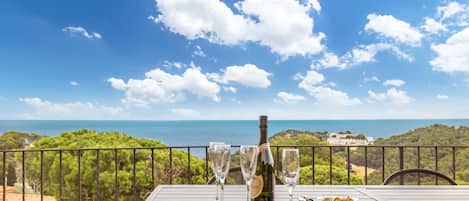 A table with a bottle and glasses on a balcony overlooking a scenic view.