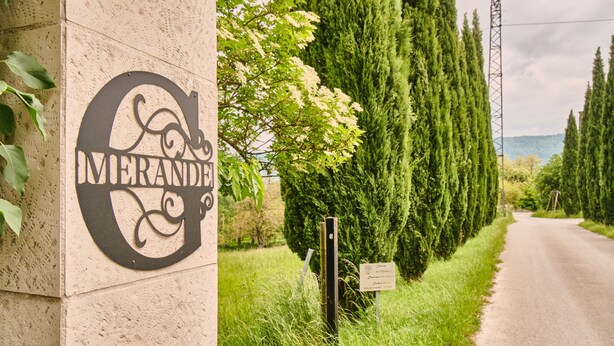 A sign with the word 'MERANDINE' on a building, a road with trees, and a grassy area.