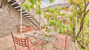 A glass-top table with metal chairs, a stone wall, and a wooden deck.