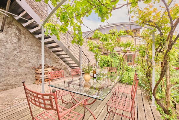 A glass-top table with metal chairs, a stone wall, and a wooden deck.