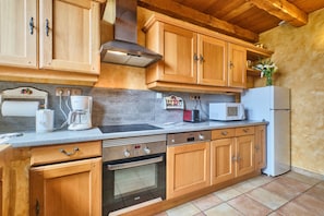 Una cucina con mobili in legno, forno a incasso, microonde e frigorifero.