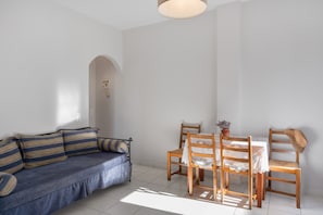 Um quarto com sofá, uma mesa de jantar com cadeiras e uma mesinha com uma planta.