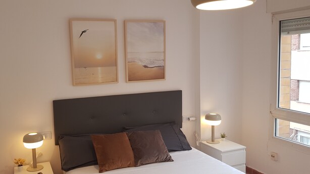 Een slaapkamer met een bed, twee aan de muur bevestigde schilderijen, bedlampen en een raam.