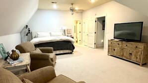 Un dormitorio con cama, televisión, cómoda y zona de estar con sofás.