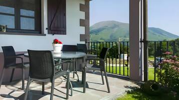 Une terrasse avec une table et des chaises, un pot de fleurs et une vue sur une colline verdoyante.