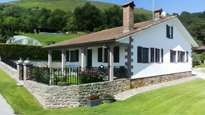 Une maison blanche avec des fondations en pierre, un toit en tuiles et une véranda couverte.