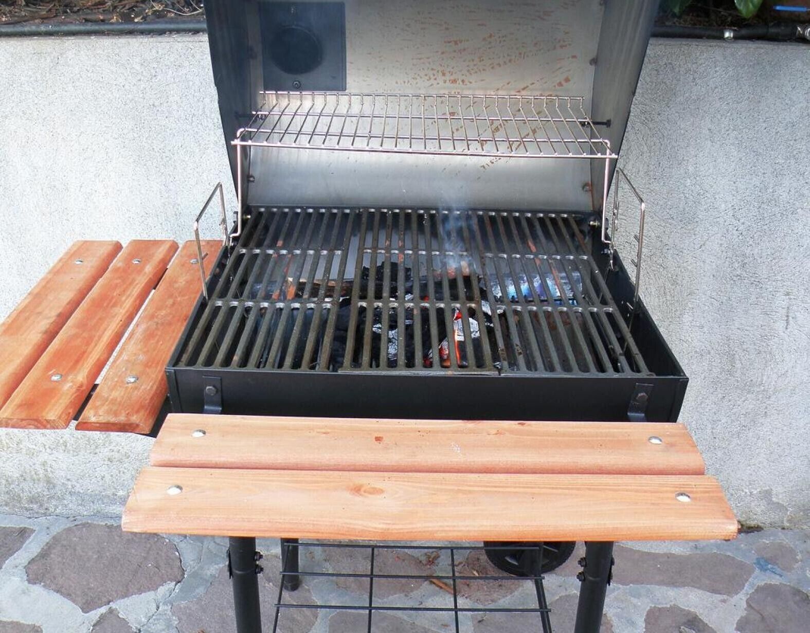 Una parrilla al aire libre con una rejilla metálica y una mesa de madera al frente.