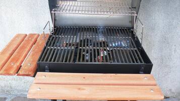 Una parrilla al aire libre con una rejilla metálica y una mesa de madera al frente.